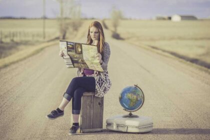 An image of a girl reading a map sitting on her suitcase in the middle of the road