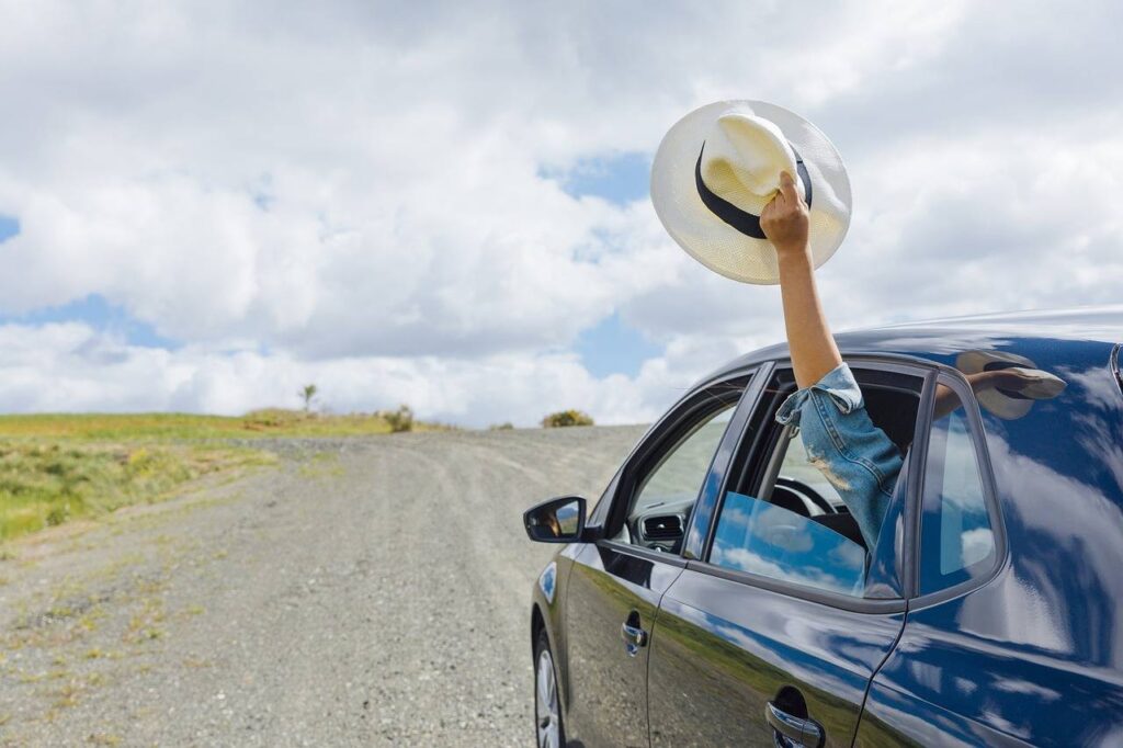 A woman removing waving a hat out of a window of a car 