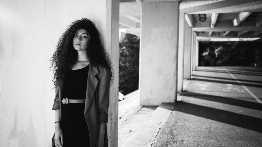 A woman with long hair standing while leaning on the wall with her back