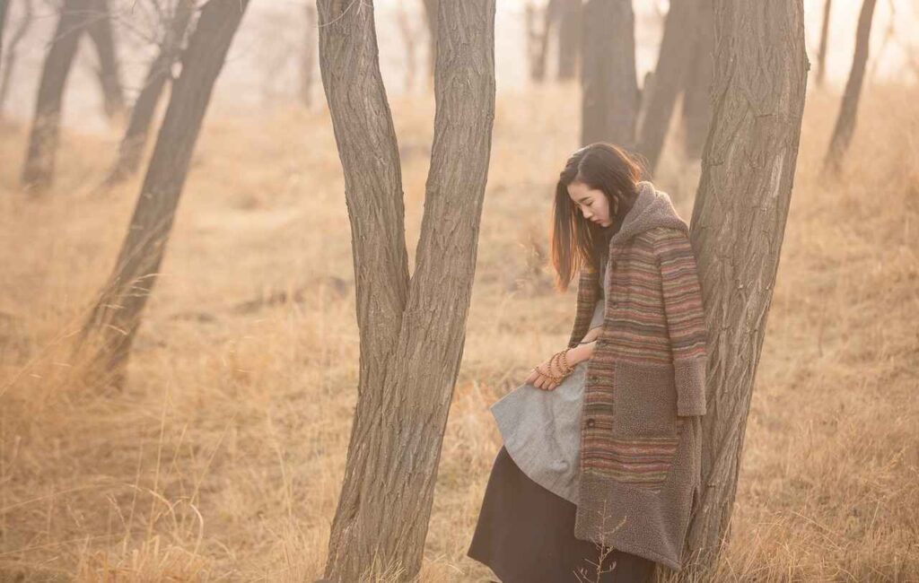 A woman in a forest alone leaning on a tree while thinking 