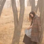 A woman in a forest alone leaning on a tree while thinking