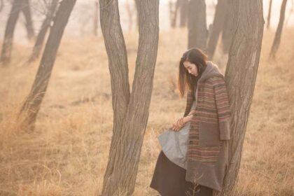 A woman in a forest alone leaning on a tree while thinking