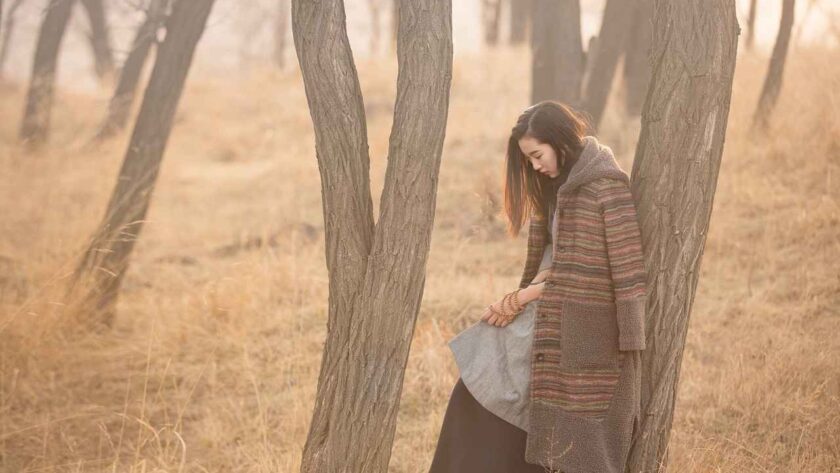 A woman in a forest alone leaning on a tree while thinking