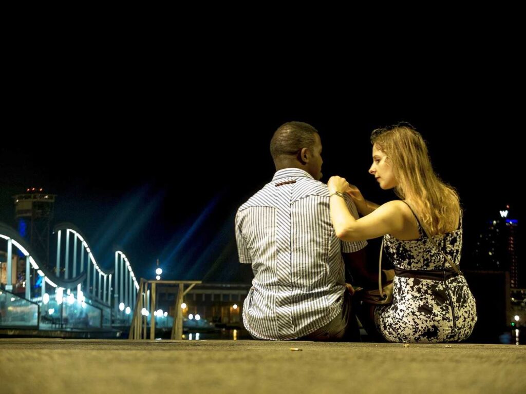 A woman sitting next to a man while putting her hands on his right shoulder as looking at him