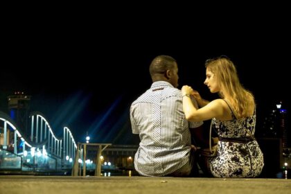 A woman sitting next to a man while putting her hands on his right shoulder as looking at him