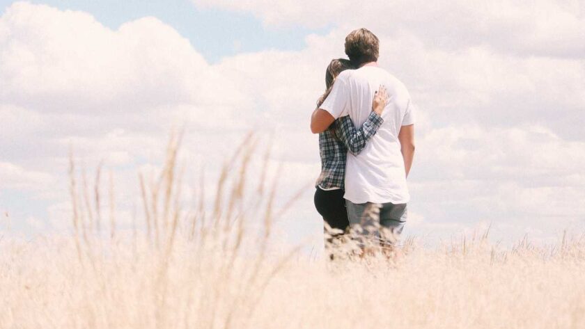 A man and a woman holding each other in open field alone