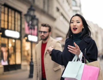 a woman holding hand her boyfriend while carrying shopping bags