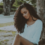 a woman sitting leaning on a tree